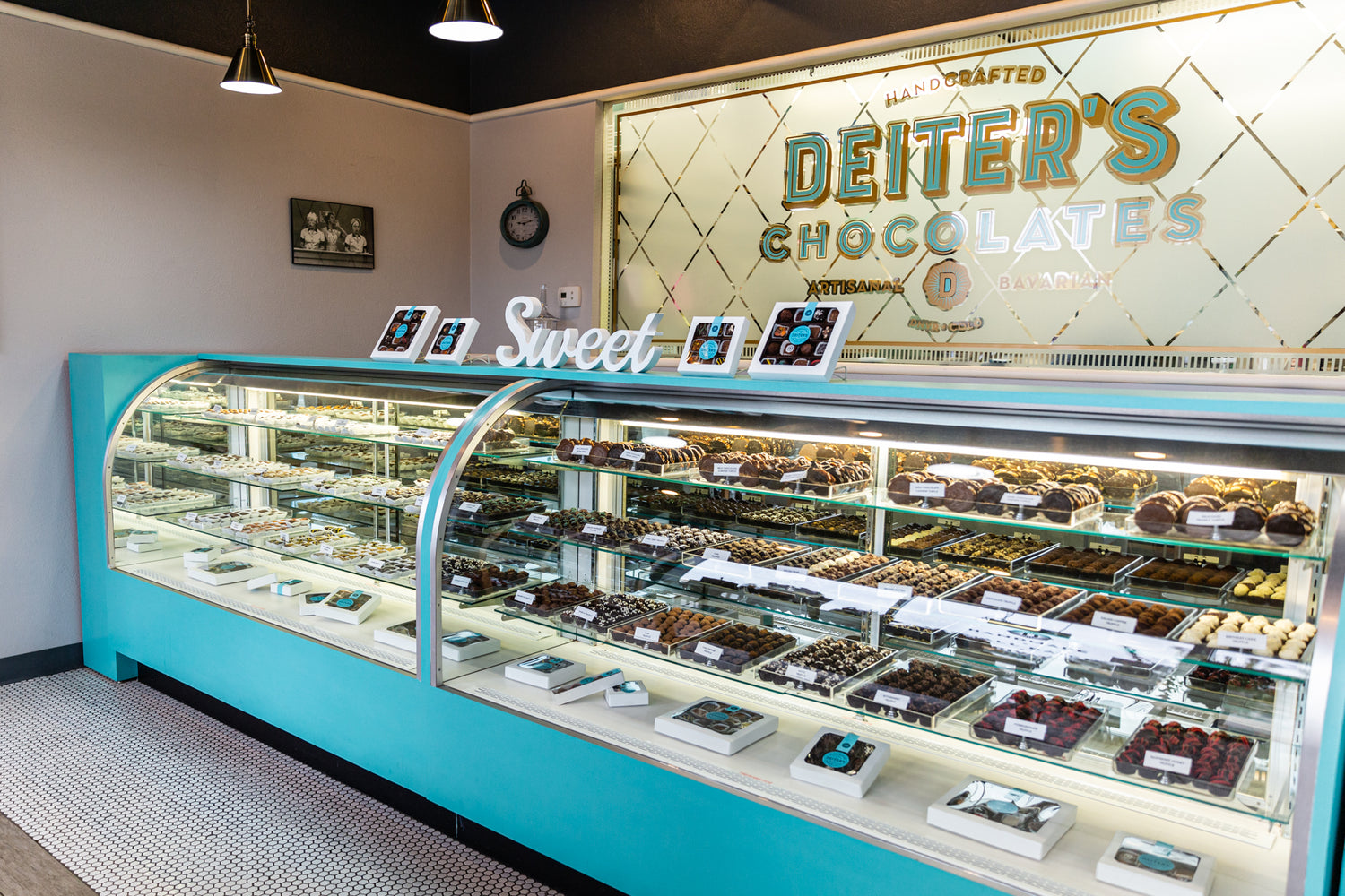 Our retro blue showcase of handcrafted truffles and caramel nut turtles sits in front of our kitchen window which features our logo. Behind the glass, our chocolatiers work in our love-worn kitchen. 