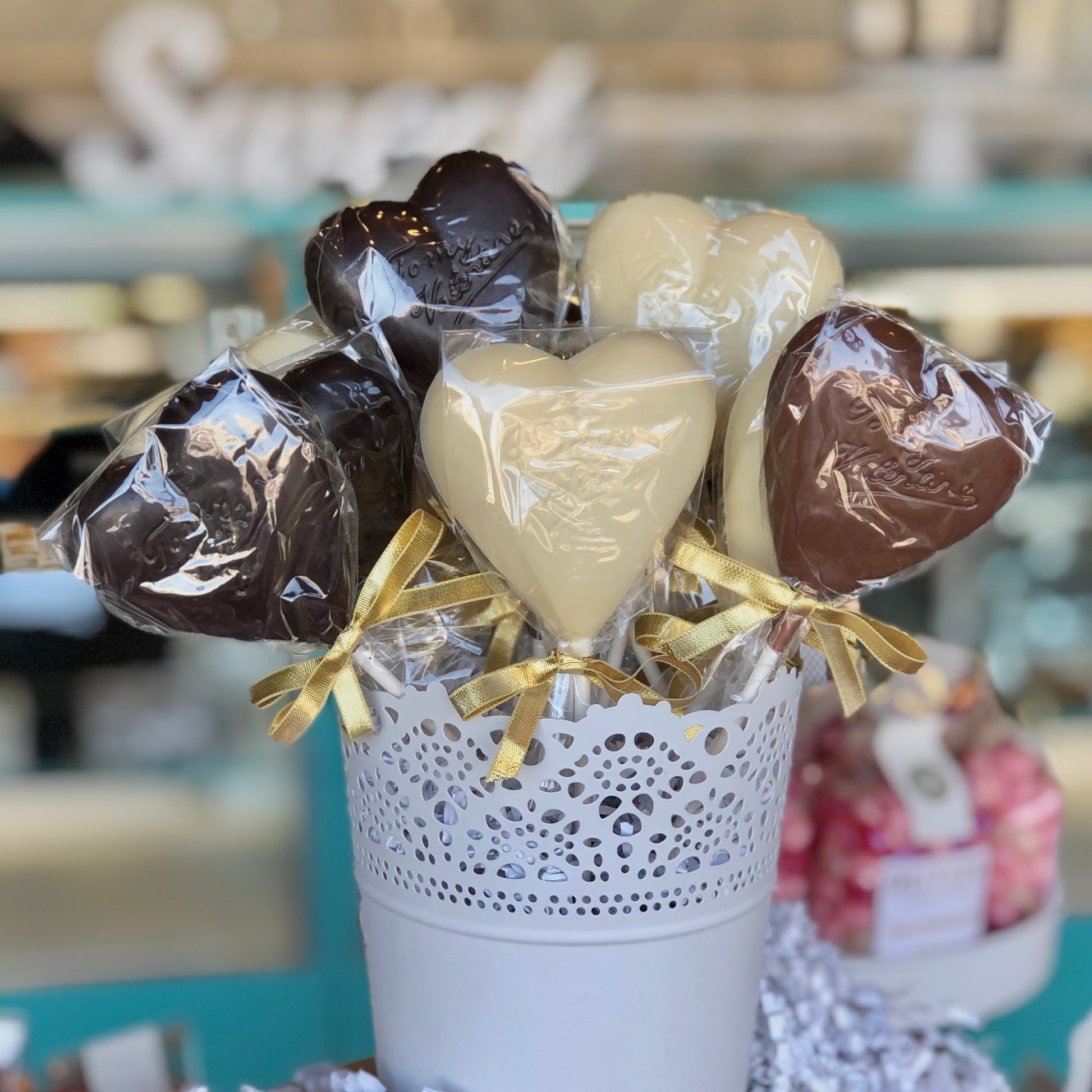 A container of milk, dark and white chocolate heart=shaped suckers wrapped with gold ribbons